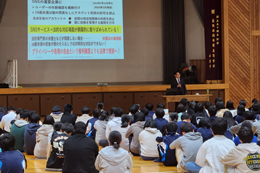 岡谷南高校の1年生を対象としたSNS講演会にて、体育館のスクリーンに映し出されたネットトラブルの事例やプライバシー設定の重要性について、講師の話を真剣に聞く生徒たちの様子。