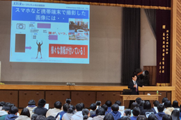 岡谷南高校の講演会風景。講師の南澤信之氏がスクリーンを使い、スマートフォンで撮影した画像に付随する位置情報などの危険性について具体的に解説している場面。