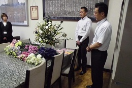 JA信州諏訪から贈られた花を前に、校内で贈呈の説明を受ける生徒と関係者の様子