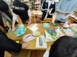 岡谷南高校の生徒たちが、机に並べられた多彩な絵本を実際に手に取りながら興味深く観察している様子