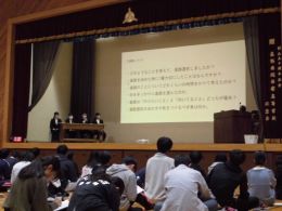 岡谷南高校のステージ上でパネルディスカッション形式により進路選択の経験を語る、4名の教育実習生と聴き入る生徒たち