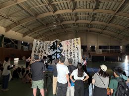 岡谷南高校の体育館にて、巨大な筆で「不撓不屈」の文字を書き上げた書道部のパフォーマンス