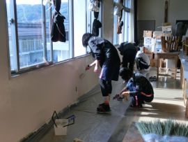 岡谷南高校：複数の生徒が協力して教室の壁を塗装している風景。床に養生シートを敷き、分担して壁面を塗り替えて教室を明るく整備している様子。