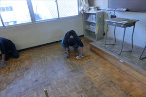 岡谷南高校：普通教室のワックスがけ。机や椅子をすべて運び出し、生徒たちが床の汚れを念入りにチェックしながら清掃している様子。