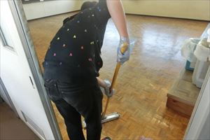 岡谷南高校：ワックスがけ専用のコーティングモップを使い、木製の床にツヤが出るよう丁寧に仕上げを行っている手元のアップ。