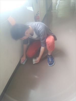 岡谷南高校：校舎の廊下にて、ハンドパットを手にした生徒が膝をつき、廊下の隅まで丁寧に汚れをこすり落としている様子。