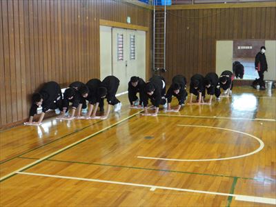 岡谷南高校：大体育館のワックスがけ。男子バスケットボール部の生徒たちが一列に並び、一斉に雑巾がけをして床を磨いている様子。
