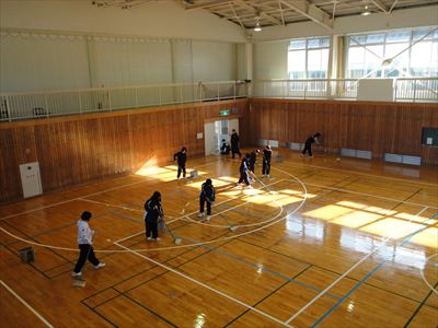 岡谷南高校：ワックスがけが完了し、窓からの光を反射して輝いている小体育館の床と、作業を終えた生徒たちの様子。