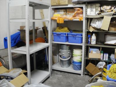 岡谷南高校：完成した頑丈なスチール棚に、清掃用具やバケツ、消耗品などが整然と収納された倉庫内の様子。