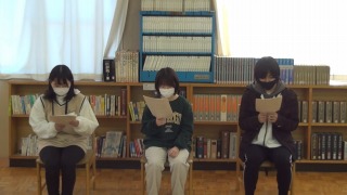 岡谷南高校の冬の読書旬間に行われた図書館朗読会。本棚を背に、椅子に座った3人の生徒が「かちかち山」などの物語を感情を込めて読み上げている様子。