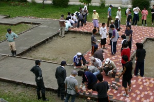 岡谷南高校：中庭の広場作り。大勢の生徒、保護者、教職員が協力し、色違いのブロックをパズルのように丁寧に敷き詰めて通路を形成していく作業風景。