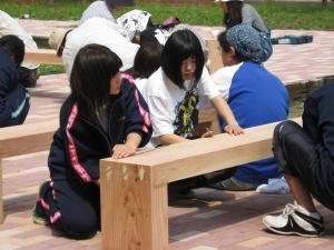 岡谷南高校：完成したばかりの木製ベンチに座り、座り心地や強度を確認しながら作業を進める生徒たちの様子。