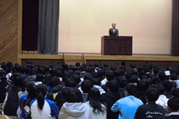 岡谷南高校の始業式にて、壇上で「飛べなくなるノミ」の話を例えに、新学期の心構えについて講話をする藤澤雅道校長先生と、それを聞く生徒たちの様子。